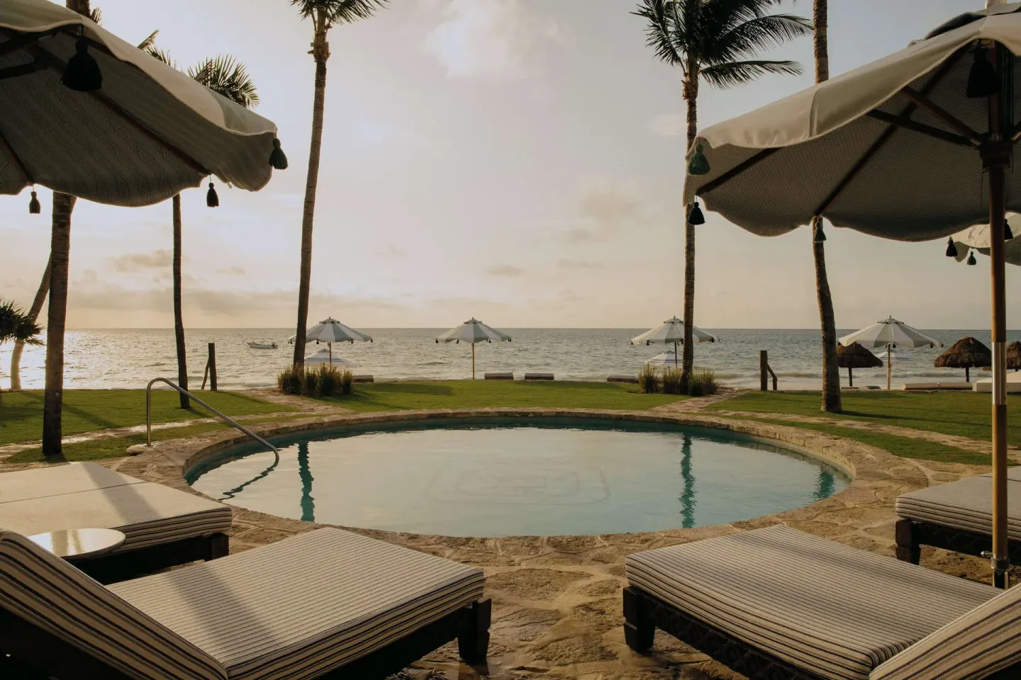 Round beachfront pool with loungers, umbrellas, palms and ocean view at Maroma, Riviera Maya.