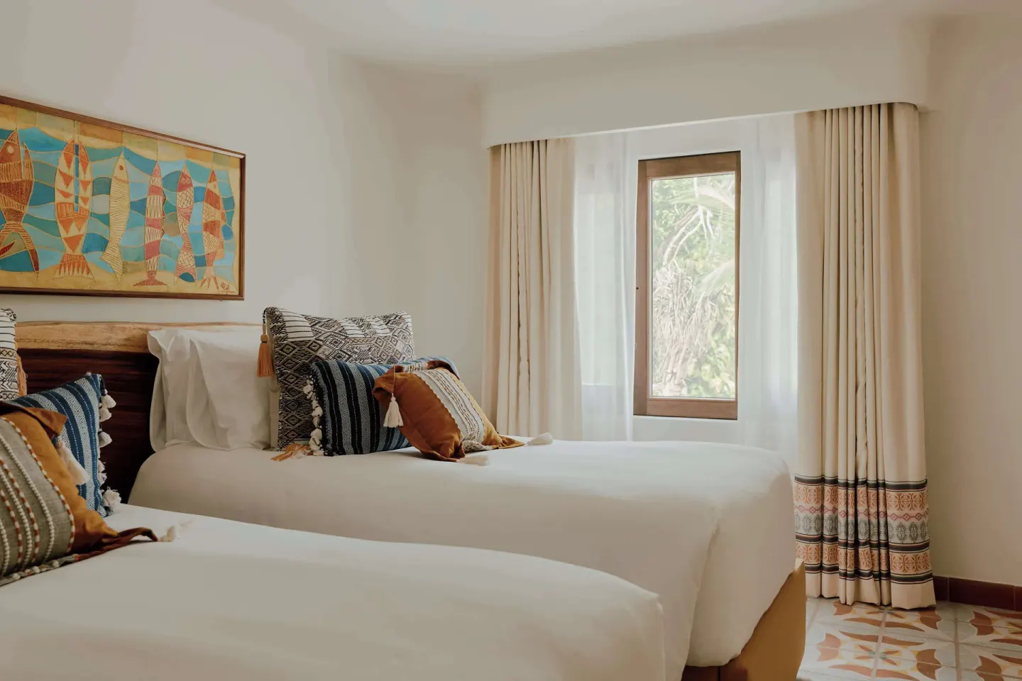 Twin beds with patterned pillows and fish artwork in a guest room at Maroma, Riviera Maya.