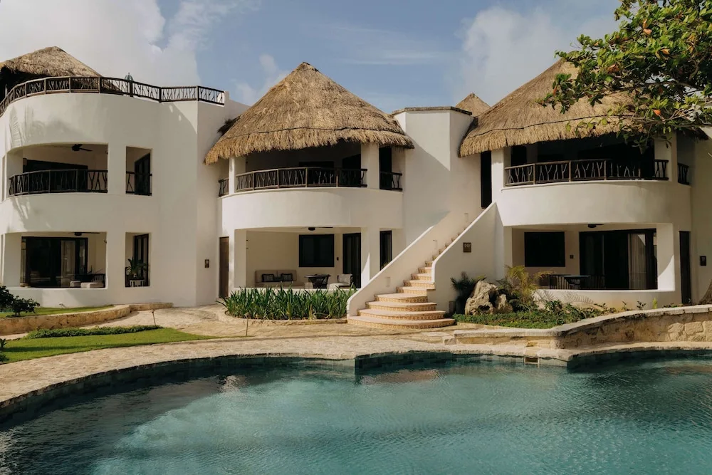 Thatched-roof resort buildings beside a pool at Maroma, Riviera Maya.
