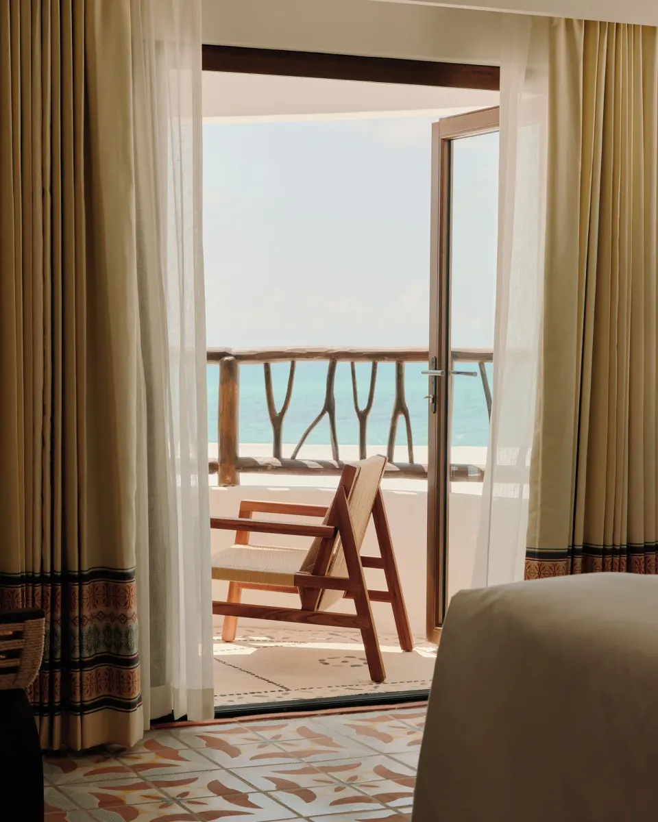 Ocean-view Deluxe Room balcony and bed at Maroma, Riviera Maya with curtains open to the sea.