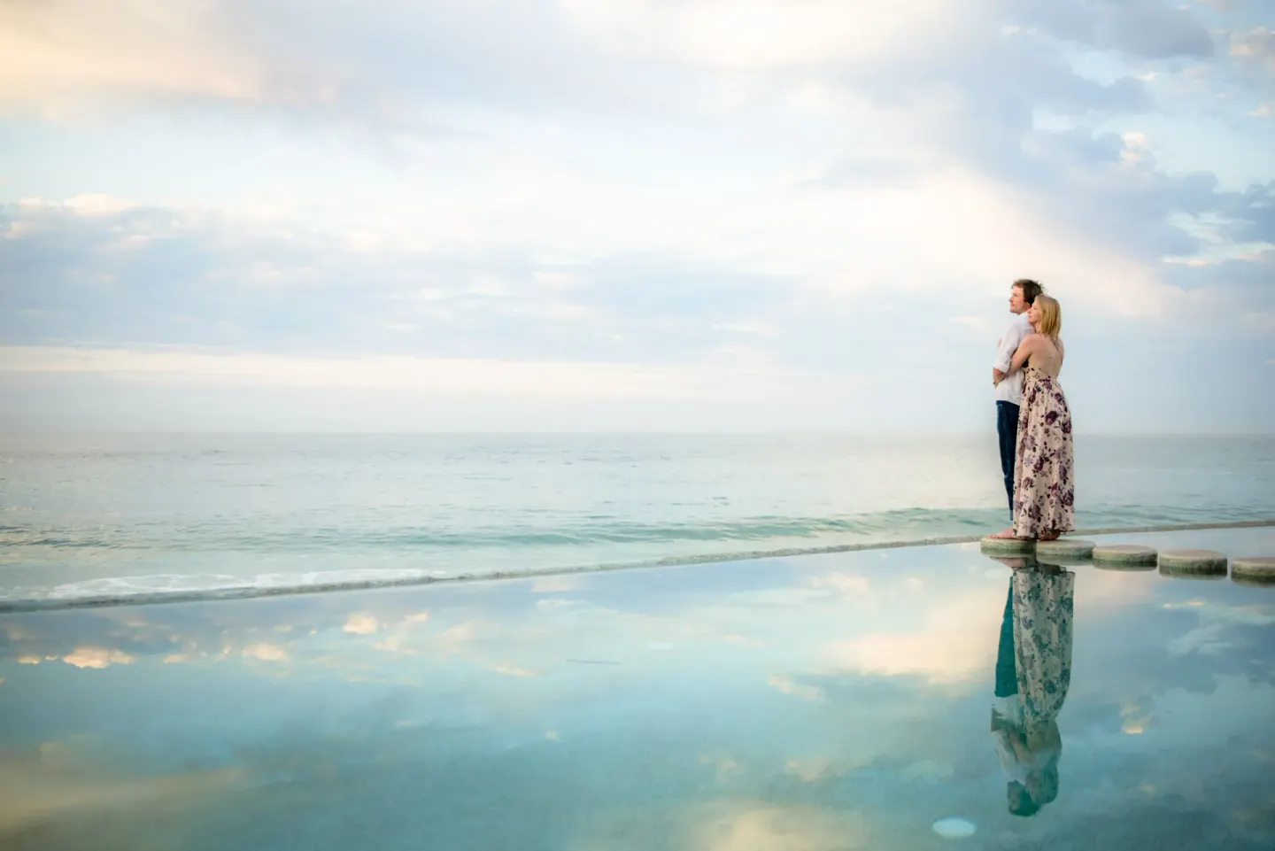 A couple stands on pool stepping stones overlooking the ocean at Marquis Los Cabos.