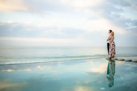 A couple stands on pool stepping stones overlooking the ocean at Marquis Los Cabos.