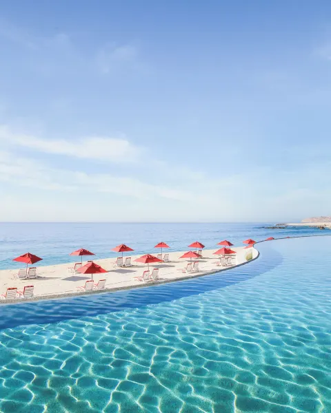 Infinity pool, beach loungers, and red umbrellas overlooking the sea at Marquis Los Cabos.
