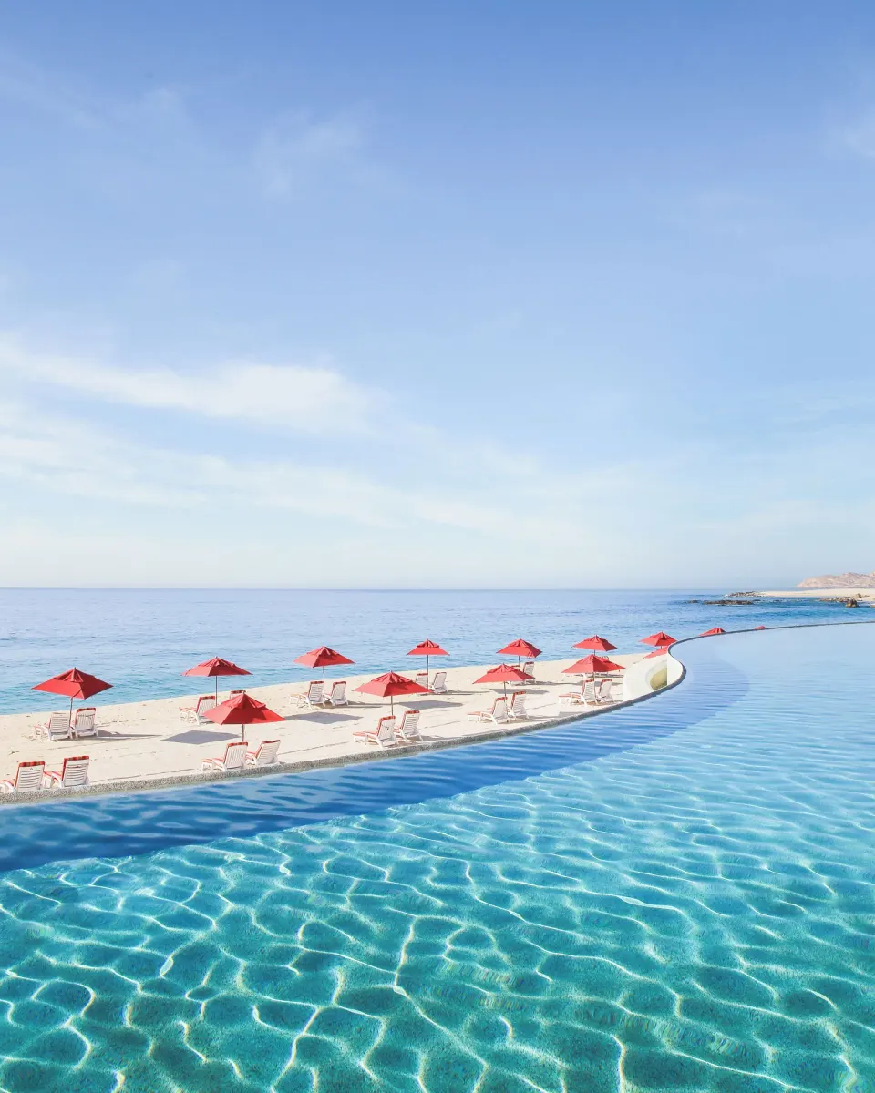 Infinity pool, beach loungers, and red umbrellas overlooking the sea at Marquis Los Cabos.