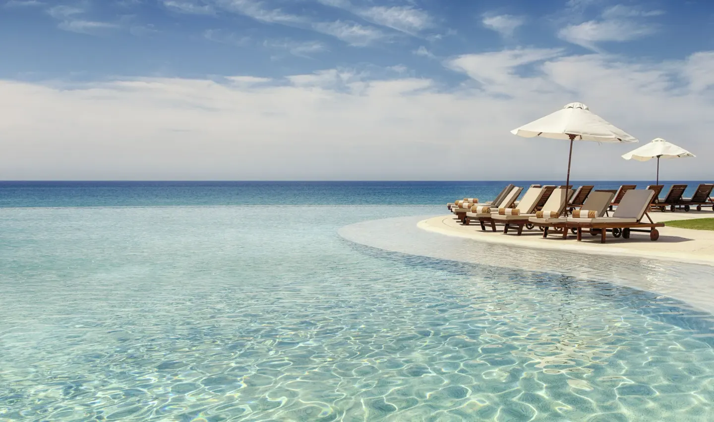 Infinity pool with lounge chairs, white umbrellas, and ocean views at Marquis Los Cabos.
