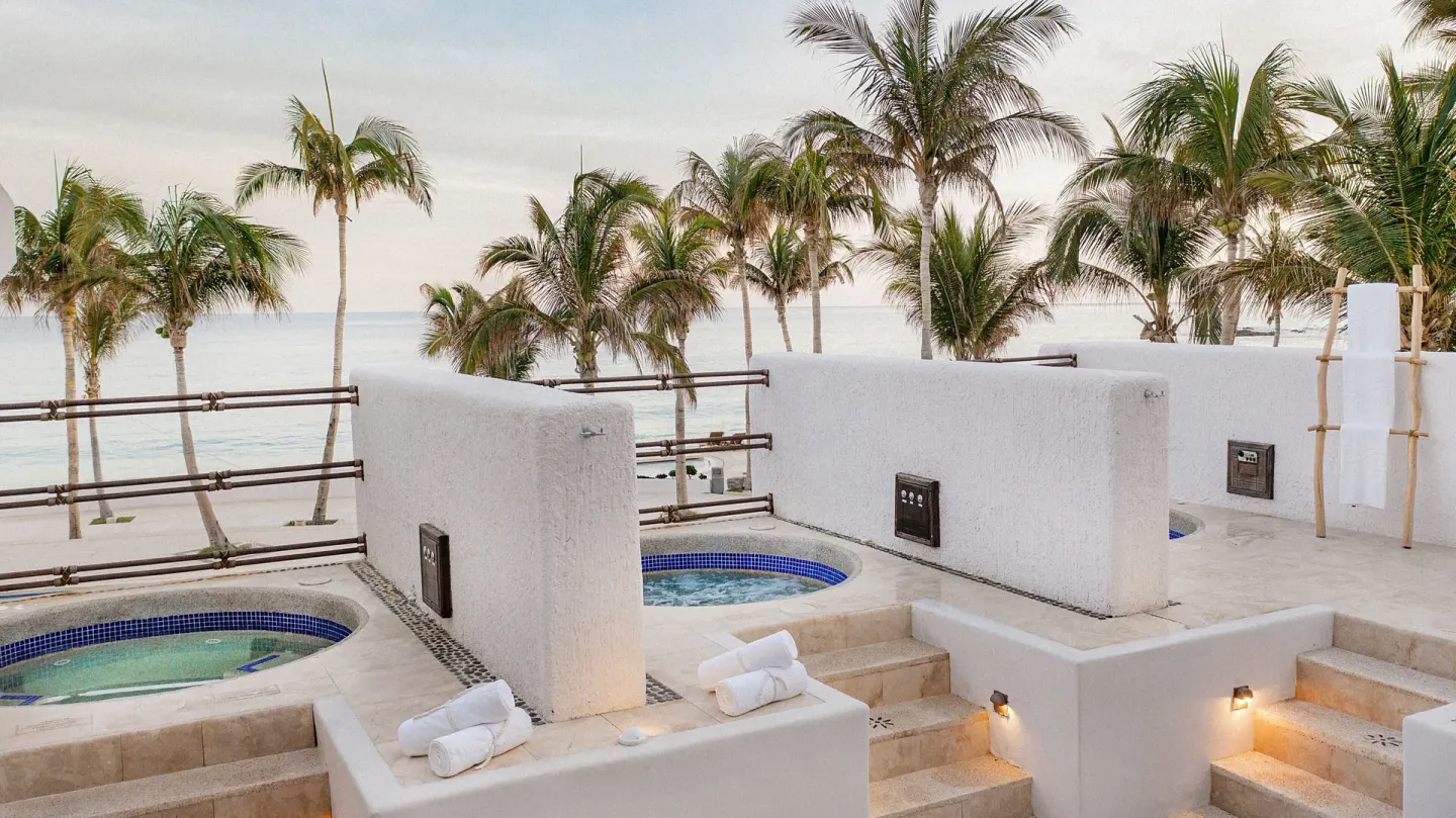 Outdoor spa tubs on a terrace with palm trees and ocean beyond at Marquis Los Cabos.