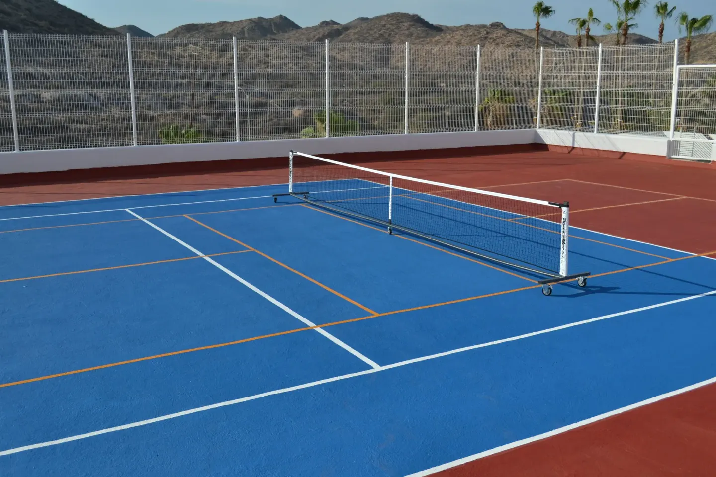Blue and red sports court with a portable net and mountain backdrop at Marquis Los Cabos.