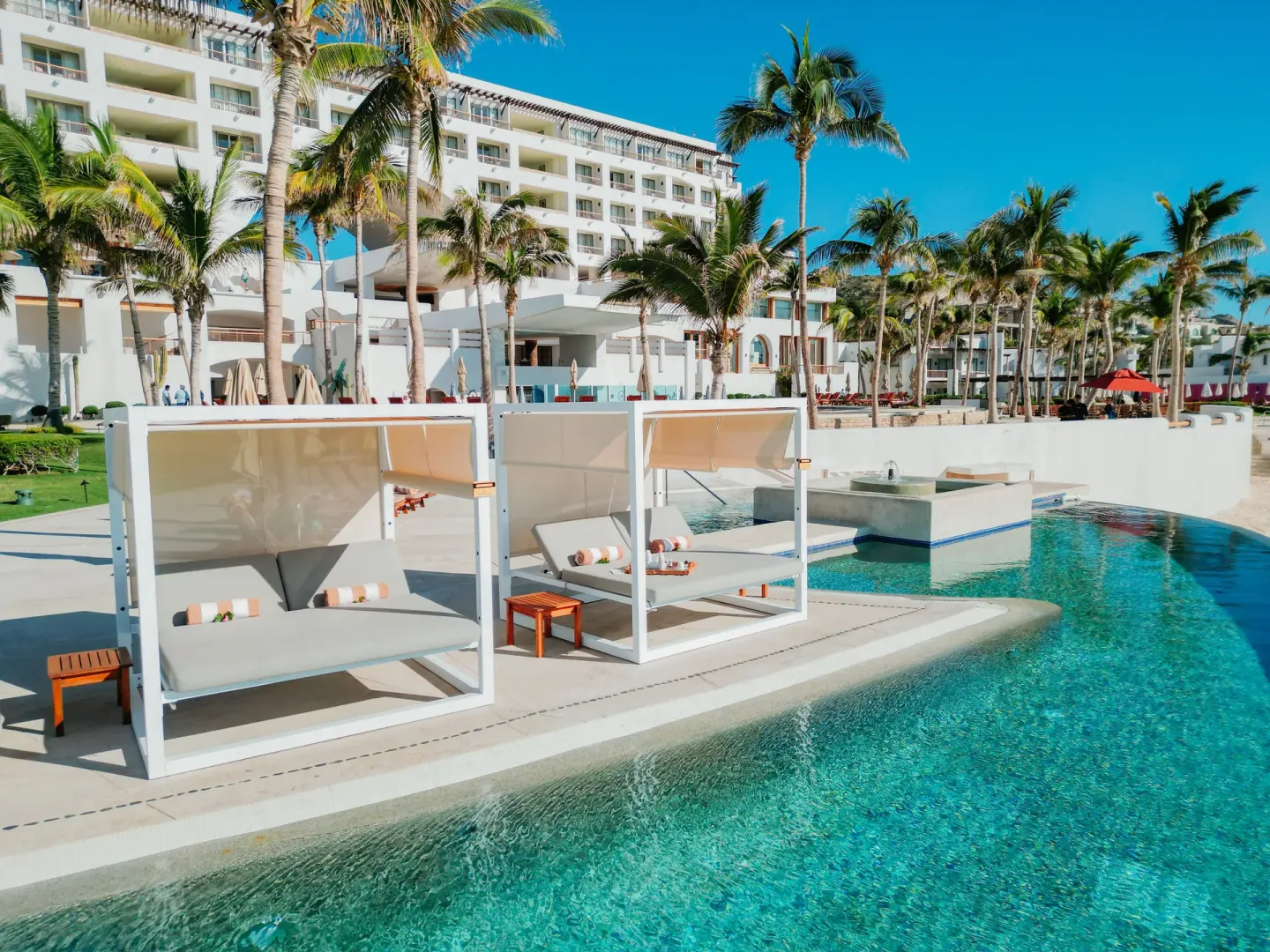 Poolside daybeds beside turquoise water and palm trees at Marquis Los Cabos.