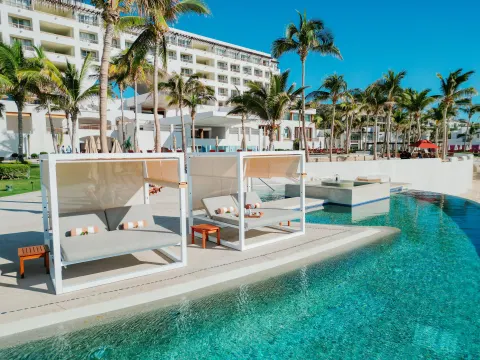 Poolside daybeds beside turquoise water and palm trees at Marquis Los Cabos.