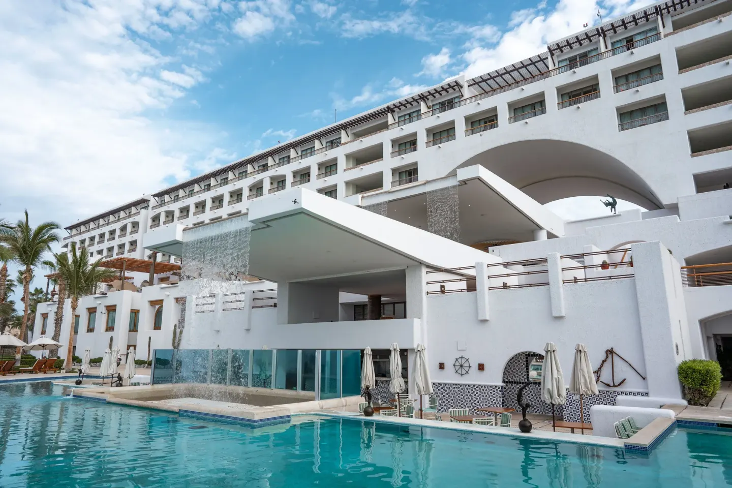 Poolside resort building with white arches and cascading water at Marquis Los Cabos.