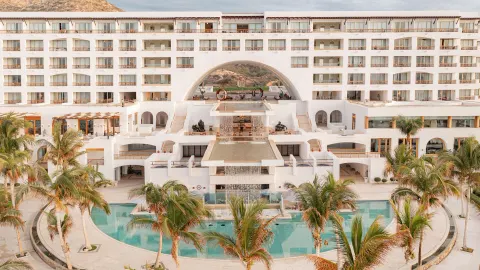Resort facade with palms, pools, and a central arch at Marquis Los Cabos.