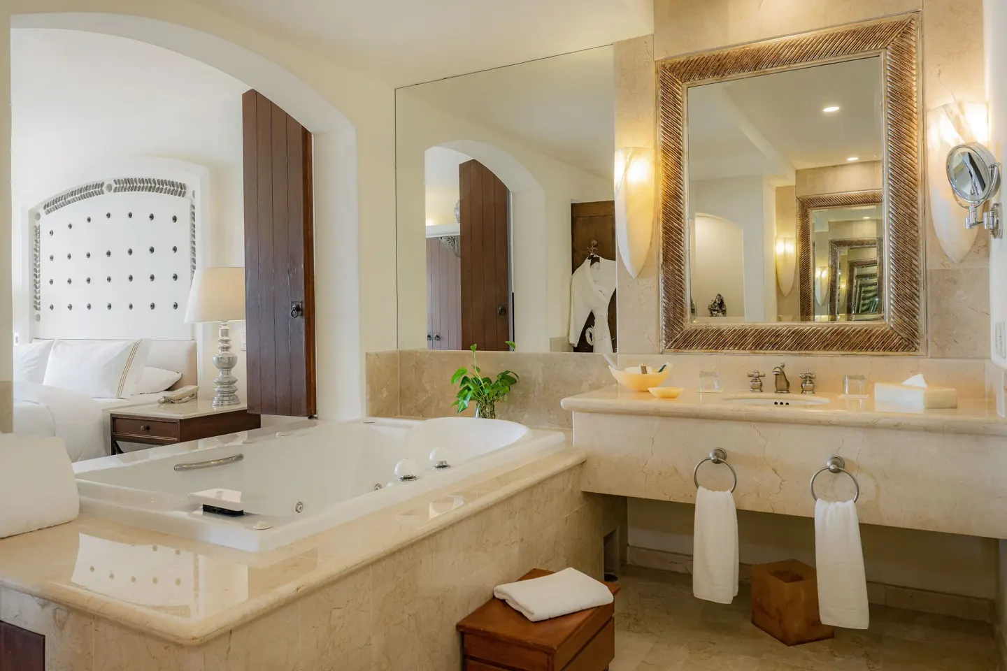 Marble bathroom with jetted tub, vanity, mirrors, and bedroom beyond at Marquis Los Cabos.