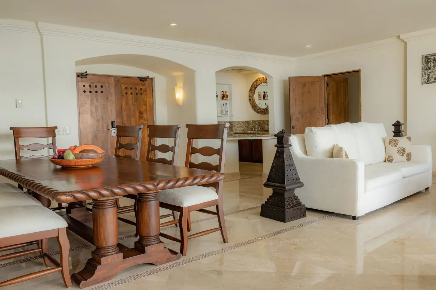 Suite dining area with wood table, white sofa, and wet bar at Marquis Los Cabos.