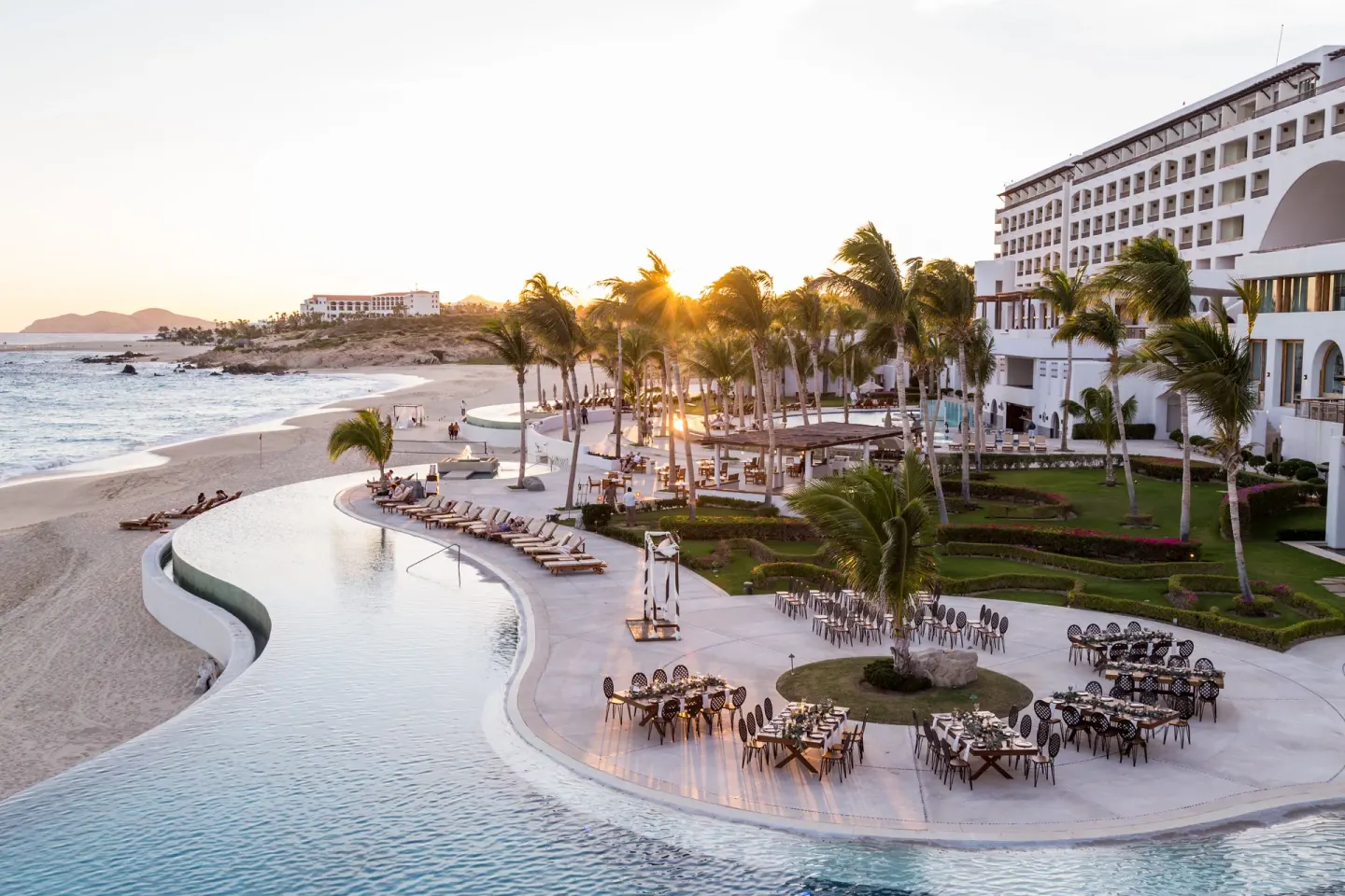 Sunset view of the pool, beach, palms, and resort buildings at Marquis Los Cabos.