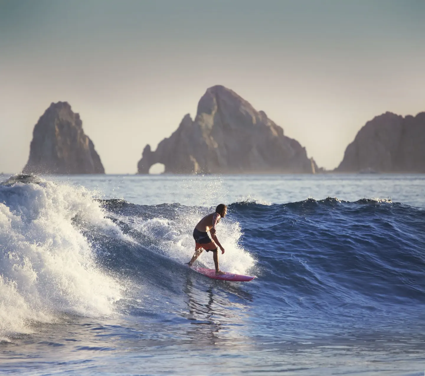 A surfer rides a wave with the Cabo rock formations offshore near Marquis Los Cabos.