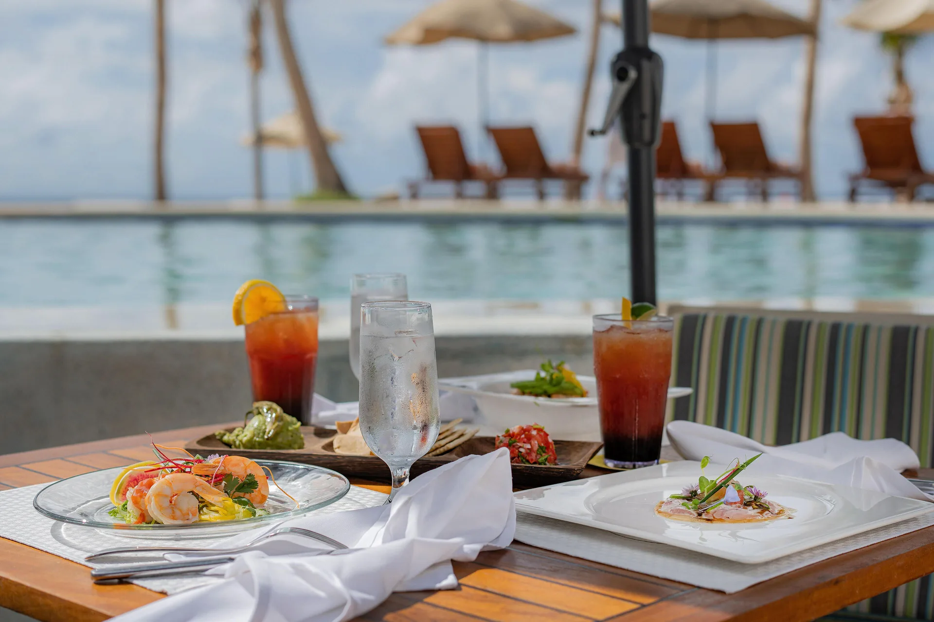 Poolside seafood plates and drinks on a table at Marquis Los Cabos.
