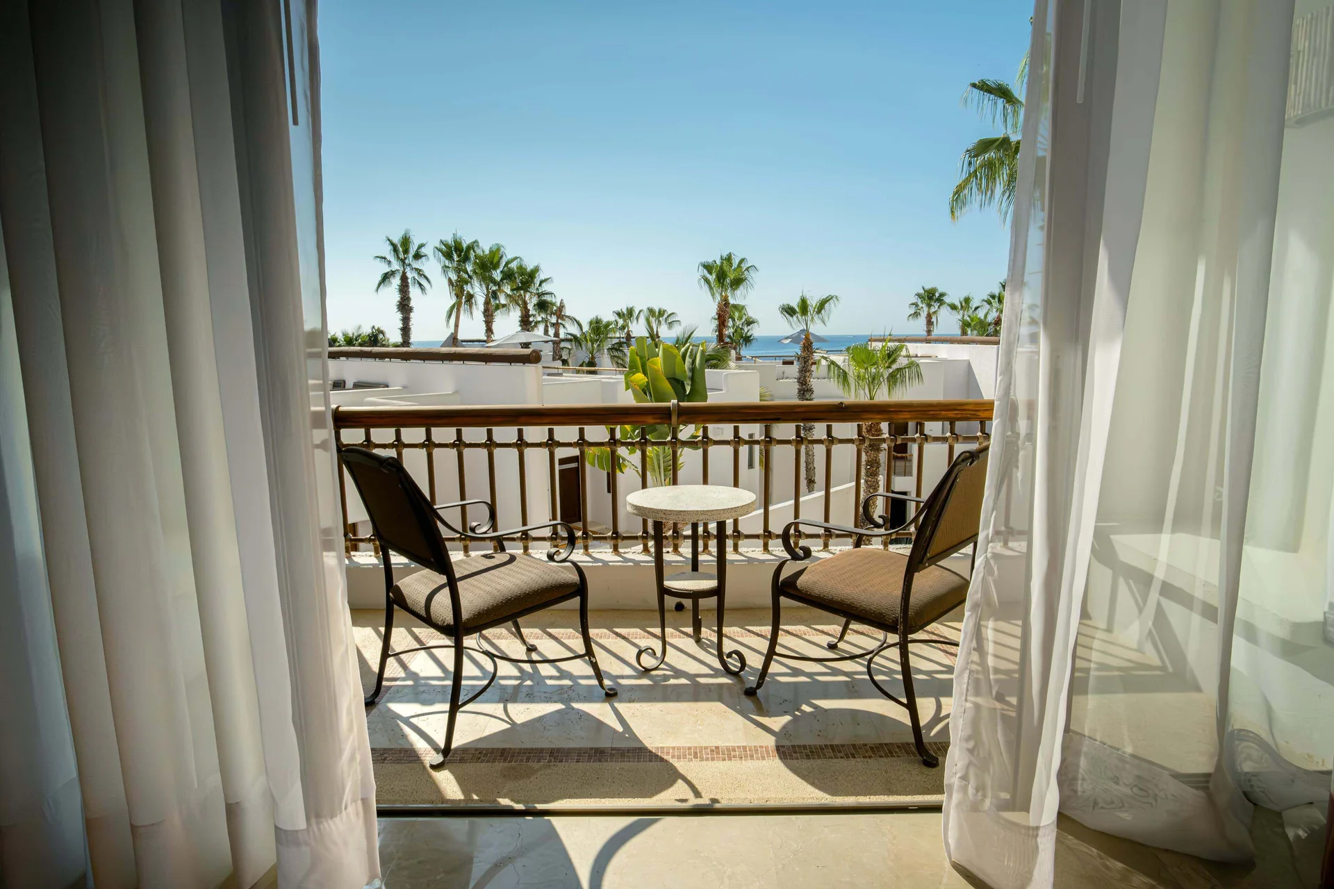 Junior Suite Eden balcony with two chairs and ocean glimpses at Marquis Los Cabos.