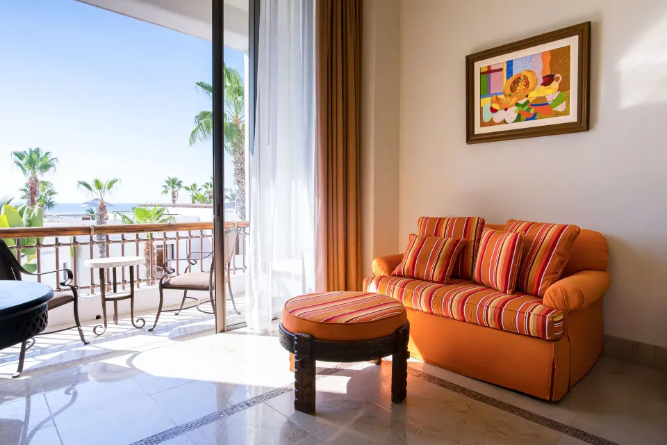 Junior Suite Eden sitting area with orange sofa and balcony view at Marquis Los Cabos.