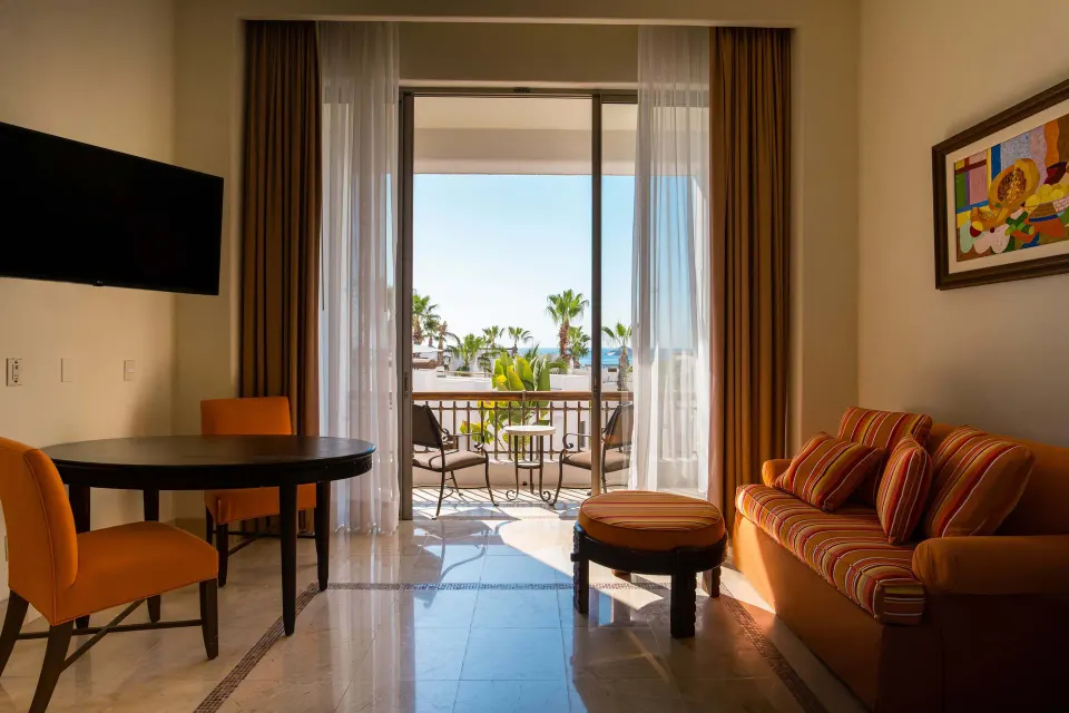 Junior Suite Eden living space with sofa, dining table, TV, and balcony at Marquis Los Cabos.