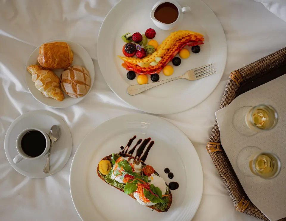 Breakfast plates on white bedding in a Junior Suite Ocean View at Marquis Los Cabos.
