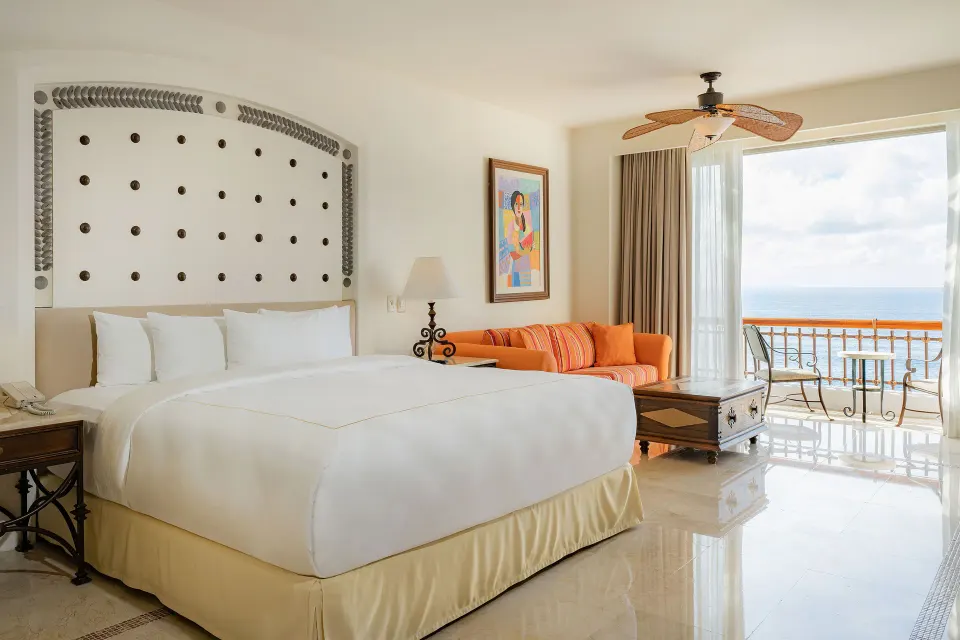 King bed in a Junior Suite Ocean View at Marquis Los Cabos with sofa and balcony beyond.