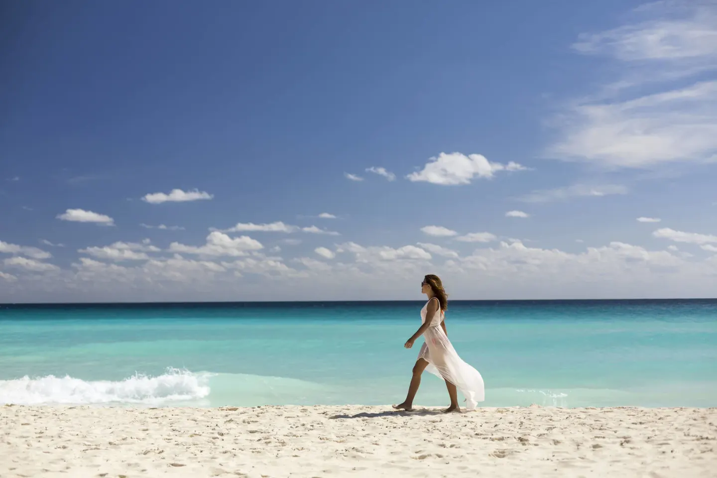 A woman walks along the white sand beach and turquoise water at Marriott Cancun.