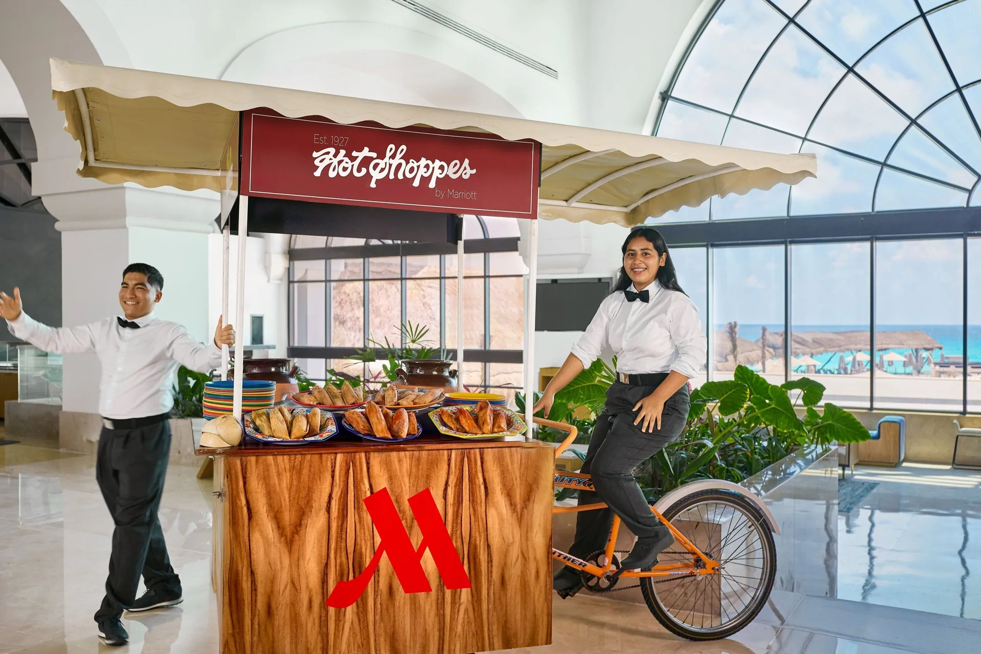 Lobby snack cart with pastries and staff beside ocean-facing windows at Marriott Cancun.