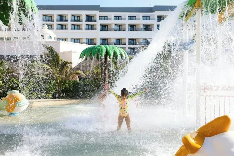 Child stands under a splash bucket in the water play area at Marriott Cancun.