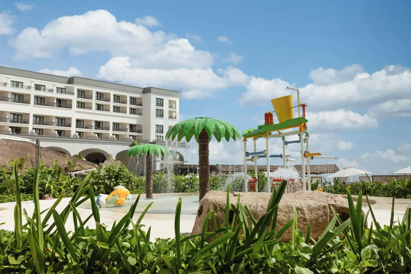 Splash pad with palm sprayers, tipping buckets, and resort building at Marriott Cancun.