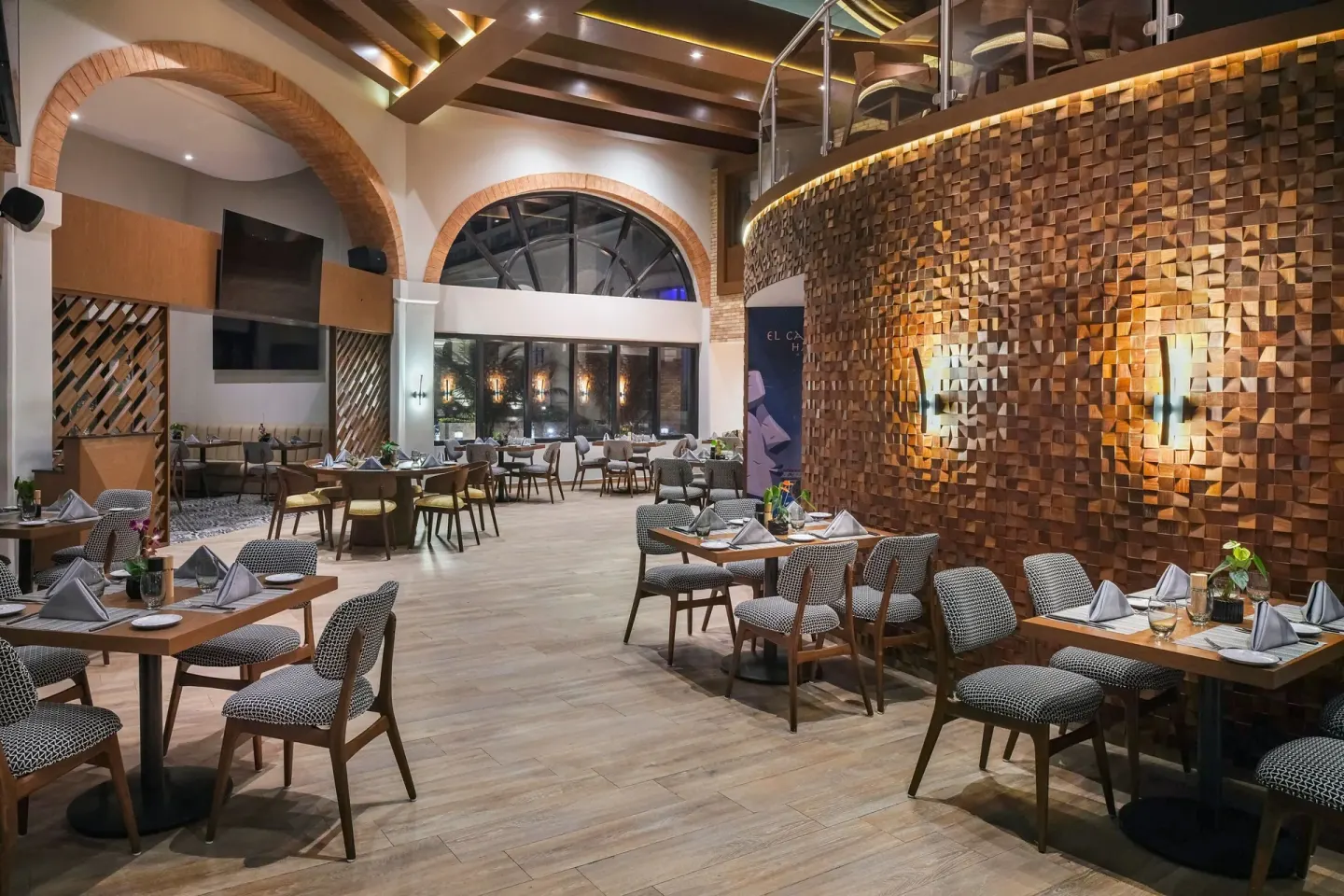 Restaurant dining room with arched windows and a textured wood wall at Marriott Cancun.