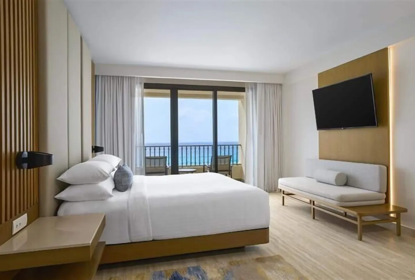 Magna Suite bedroom with king bed, sofa bench, TV, balcony, and ocean view at Marriott Cancun.
