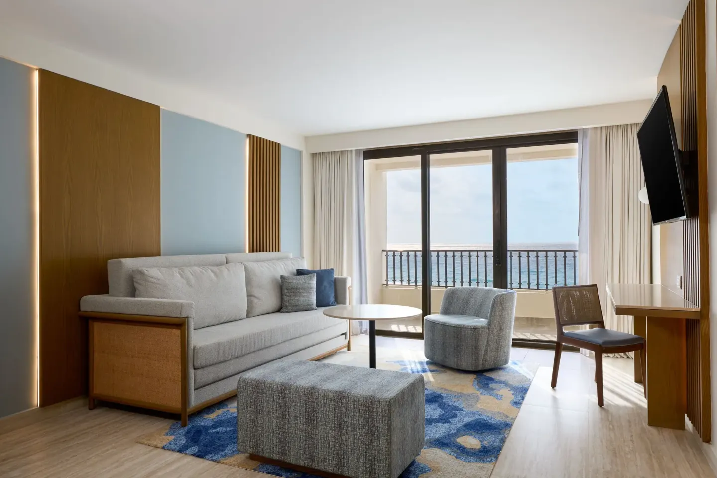 Magna Suite living room with sofa, desk, TV, balcony, and ocean view at Marriott Cancun.