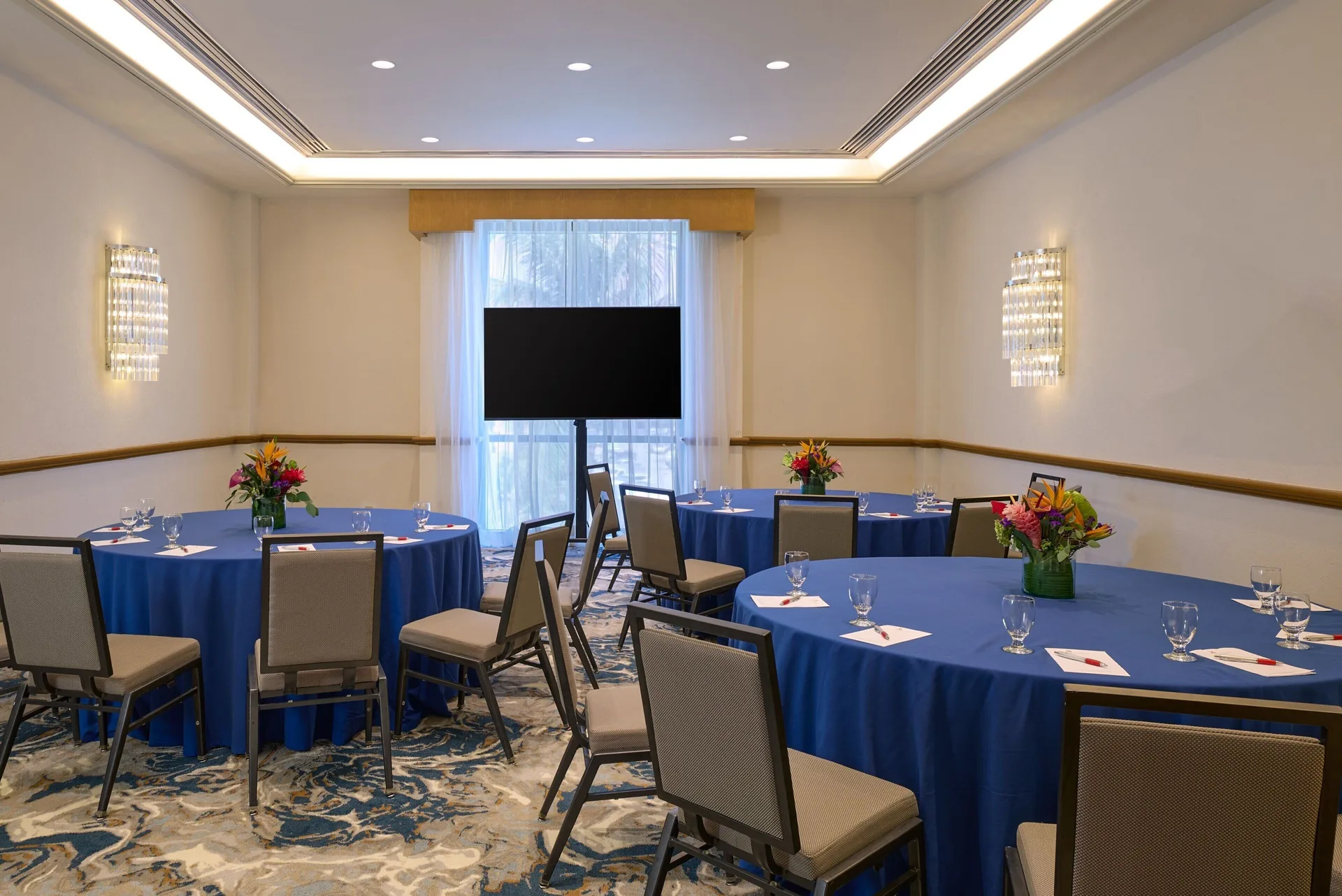 Meeting room with round blue-clothed tables and a display screen at Marriott Cancun.