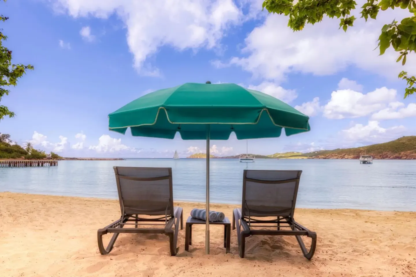 Beach loungers under a green umbrella by calm water at Marriott's Frenchman's Cove.