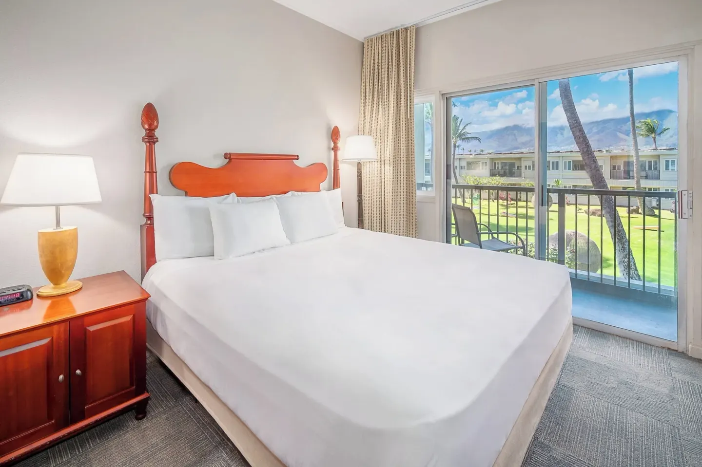 King bed guest room with balcony view of hotel grounds and mountains at Maui Beach Hotel.