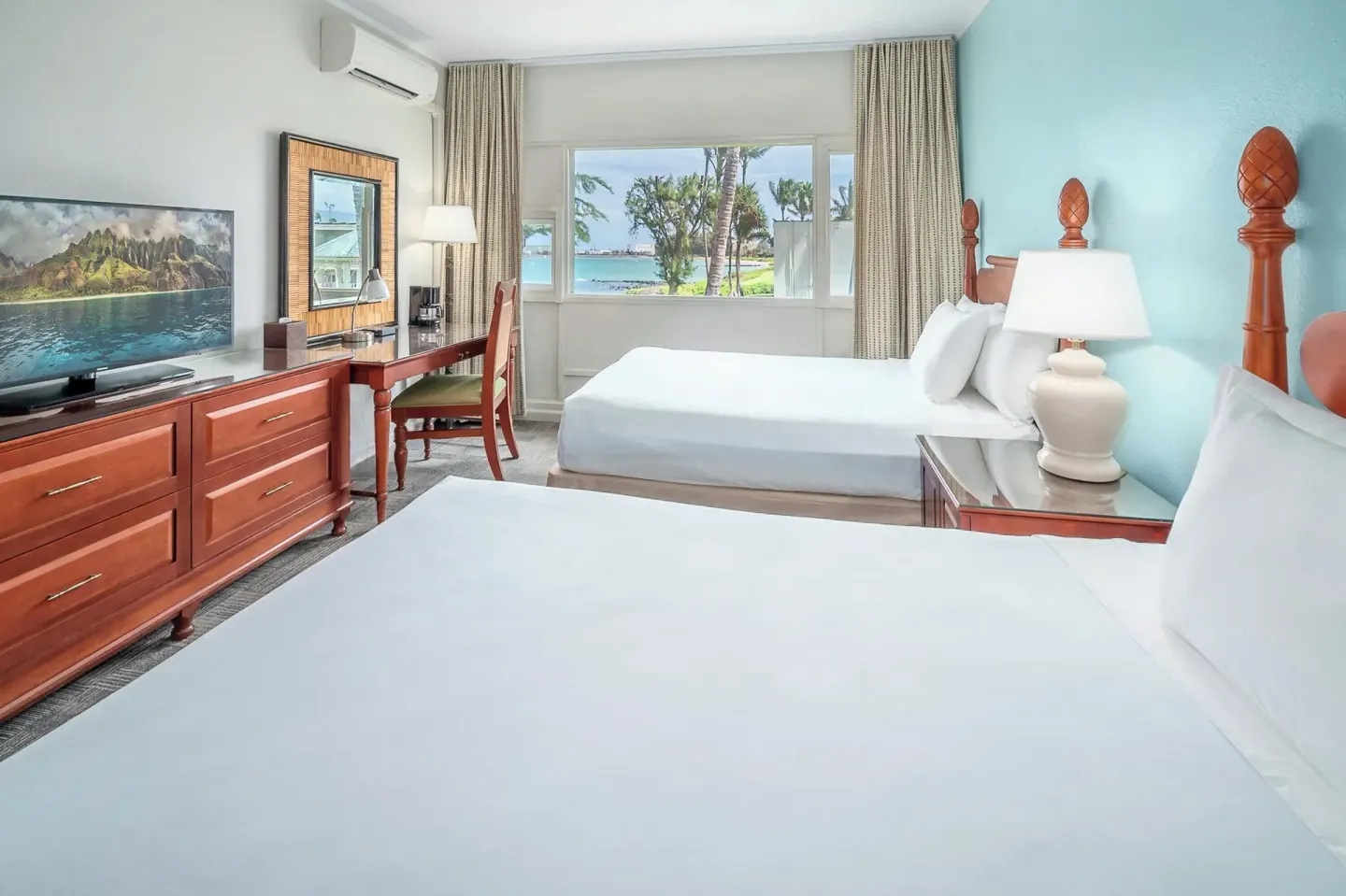 Two-bed guest room with turquoise accent wall and garden view at Maui Beach Hotel.