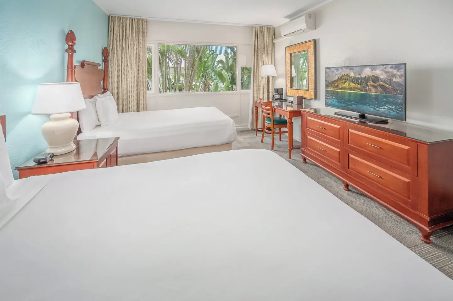 Two-bed guest room with dresser, TV, desk, and garden-facing window at Maui Beach Hotel.