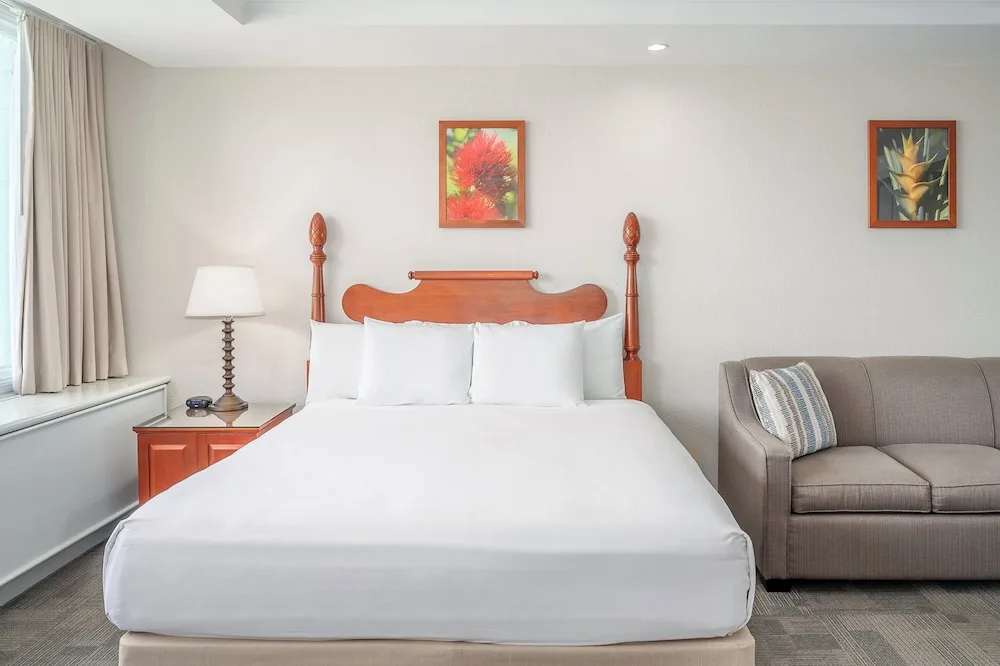 King bed guest room with sofa, bedside lamp, and floral wall art at Maui Beach Hotel.