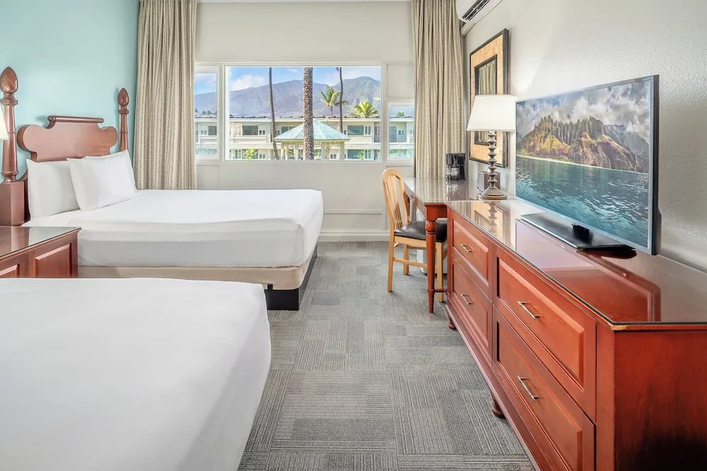 Two-bed guest room with desk, dresser, and mountain view at Maui Beach Hotel.