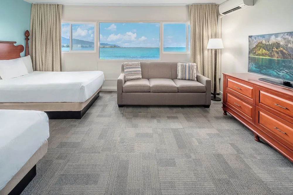 Two-bed guest room with sofa, TV, and ocean view windows at Maui Beach Hotel.