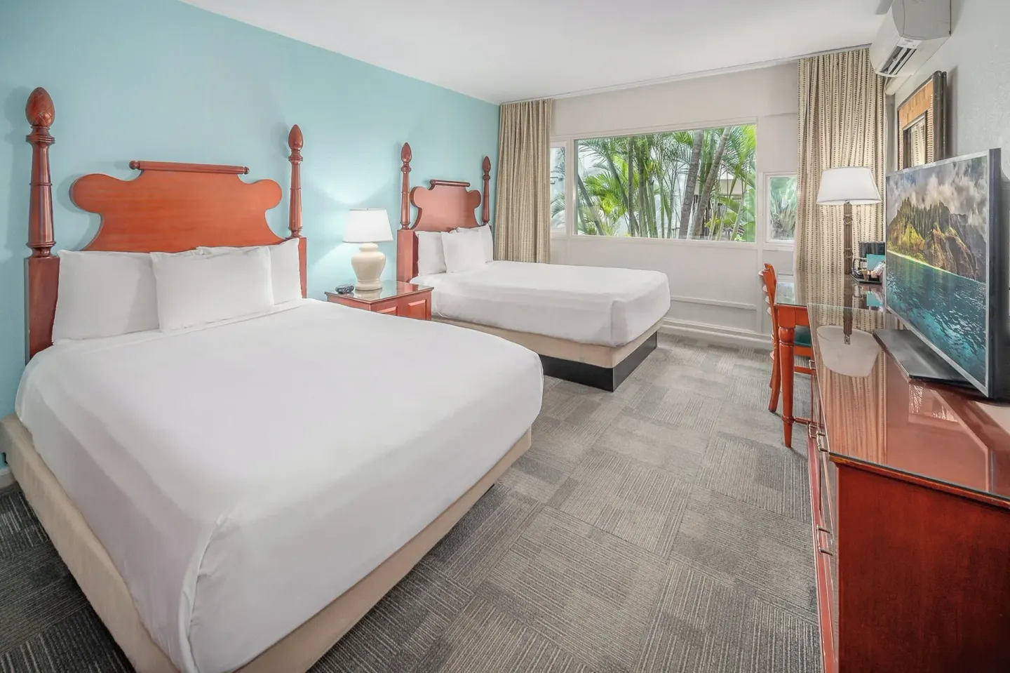 Two-bed guest room with blue wall, TV, desk, and palm views at Maui Beach Hotel.
