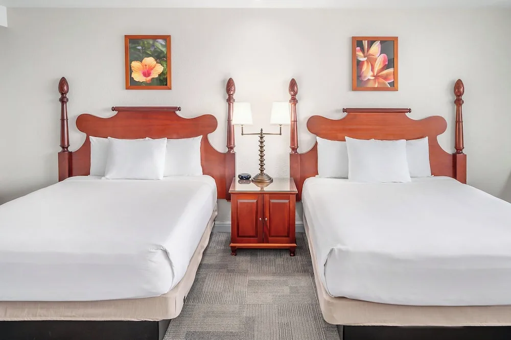 Two white beds with wood headboards and floral artwork in a guest room at Maui Beach Hotel.