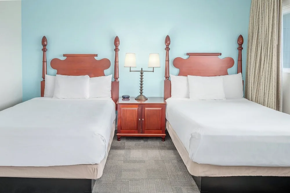 Two white beds with wood headboards and a shared nightstand at Maui Beach Hotel.