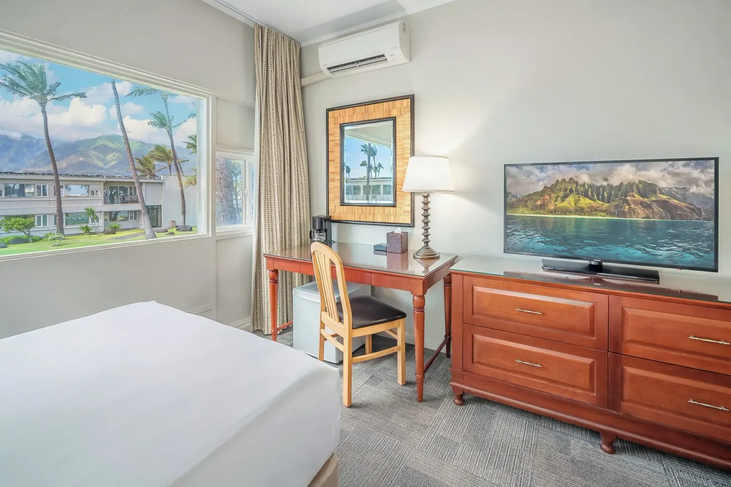 Guest room desk and dresser beside a window with palms at Maui Beach Hotel.