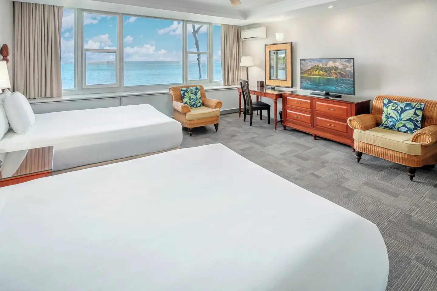 Two-bed guest room with ocean windows, desk, TV, and lounge chairs at Maui Beach Hotel.