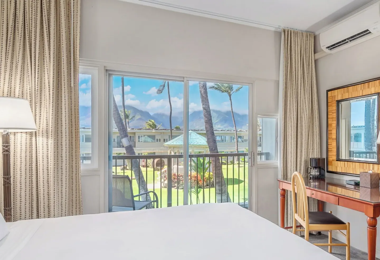 Garden View One room at Maui Beach Hotel with bed, balcony, desk, and lawn view through sliding doors.