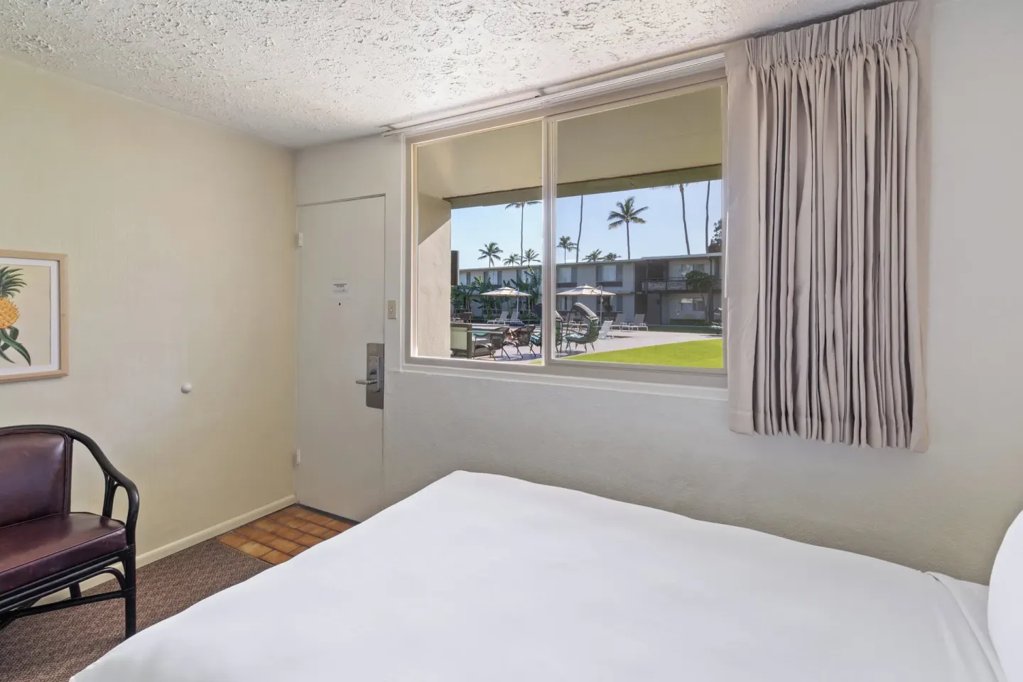 Guest room bed beside a window overlooking the courtyard at Maui Seaside Hotel.