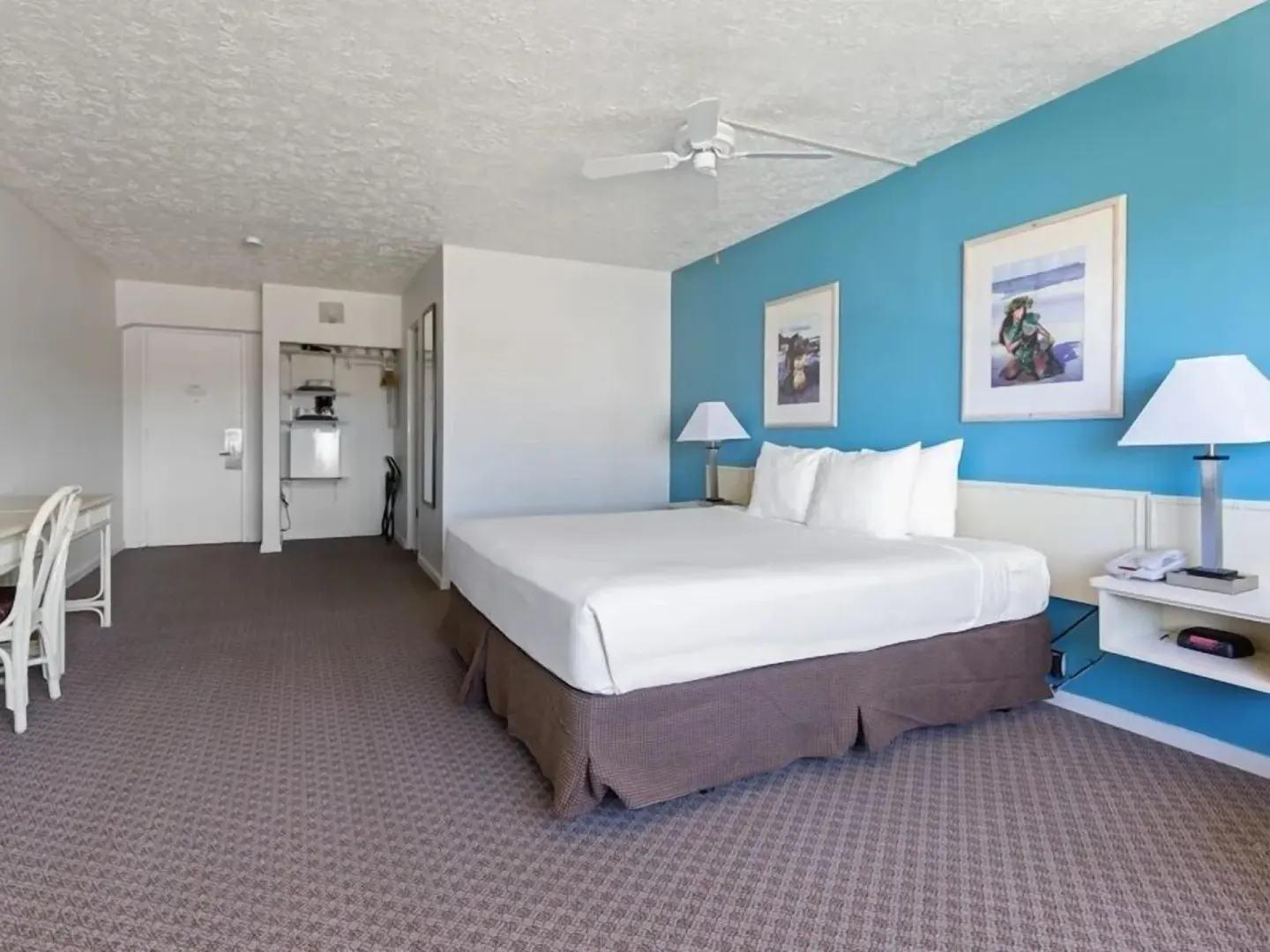 Guest room with king bed, blue accent wall, desk, and open closet at Maui Seaside Hotel.