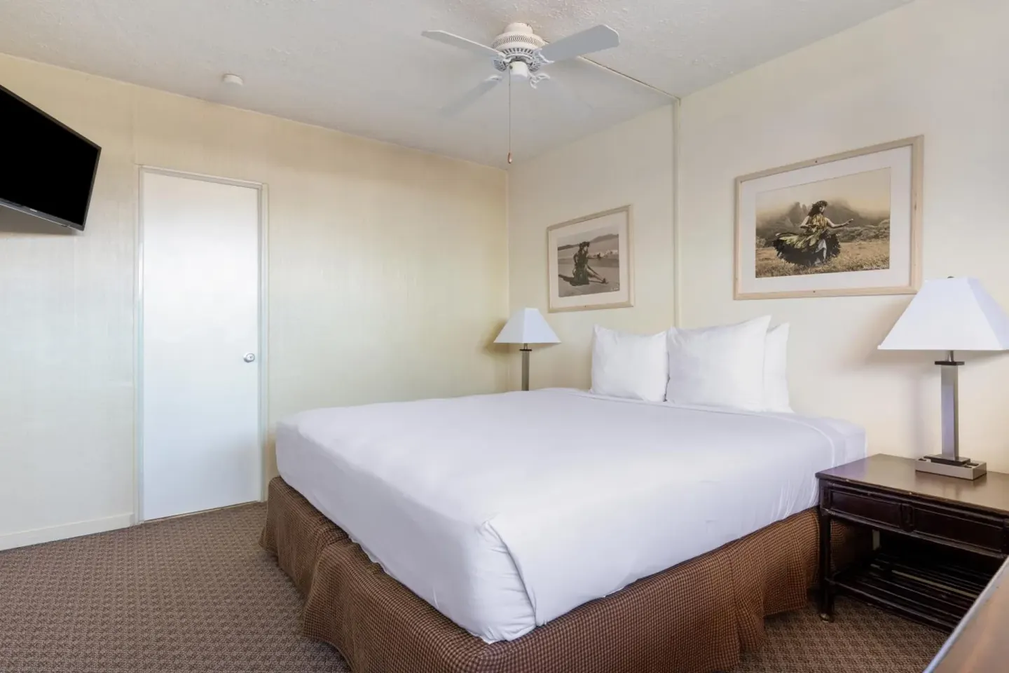 Guest room with one king bed, wall-mounted TV, ceiling fan, and lamps at Maui Seaside Hotel.