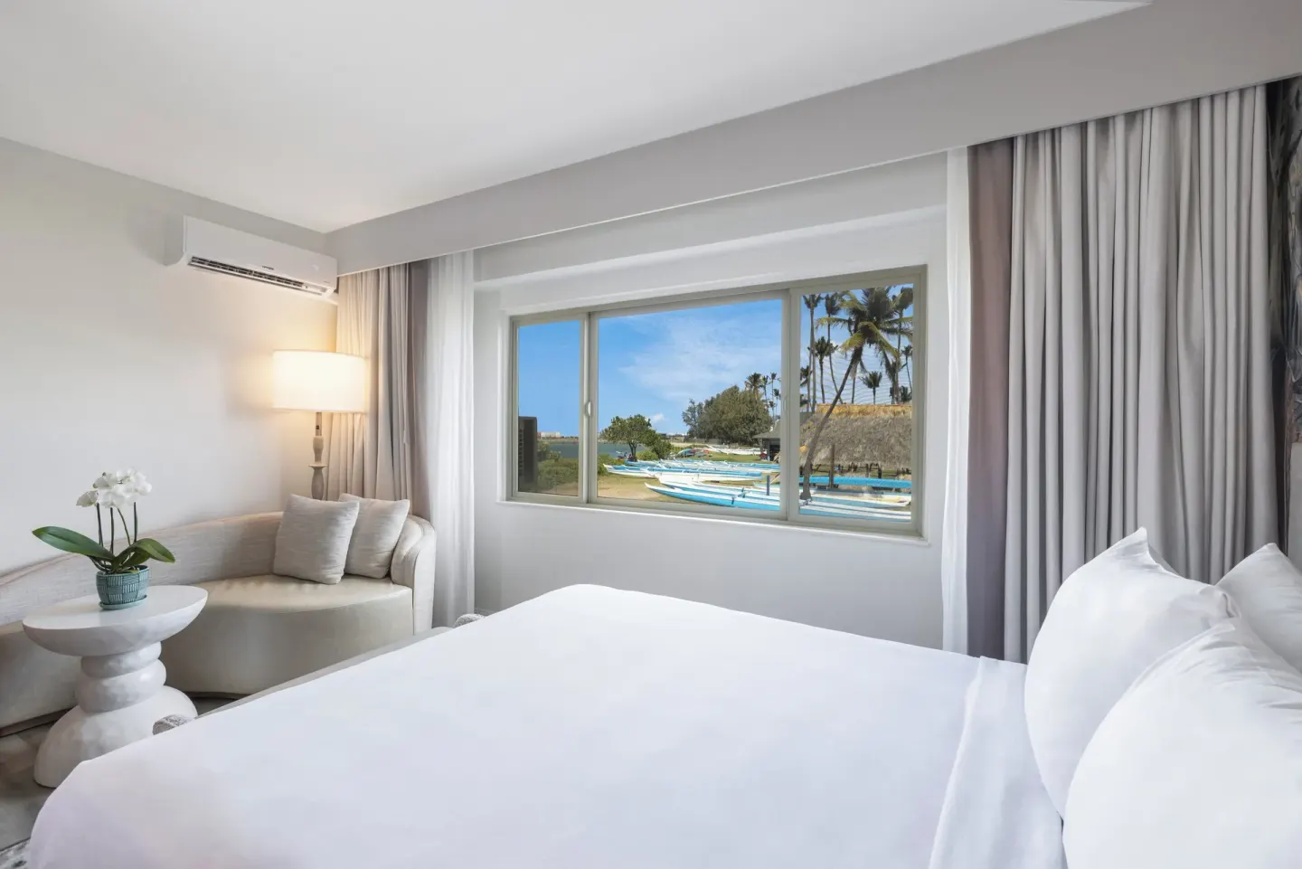 King bed guest room with sitting chair and window view of canoes at Maui Seaside Hotel.